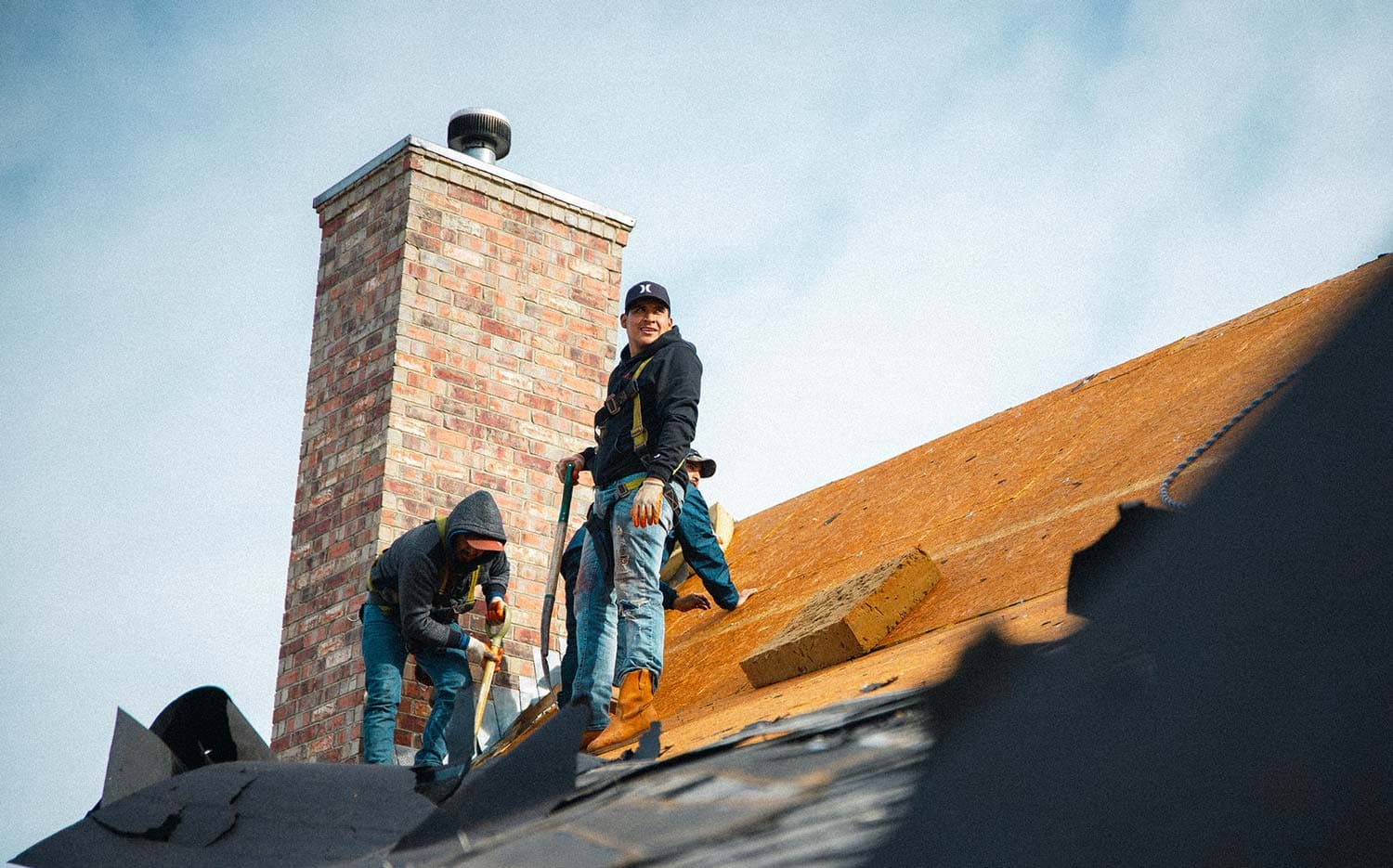Roofing crew removing old shingles before deck inspection